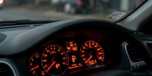 Gros plan réaliste du tableau de bord d’une voiture avec le voyant d’injection moteur allumé, ambiance automobile sombre et éclairage feutré.